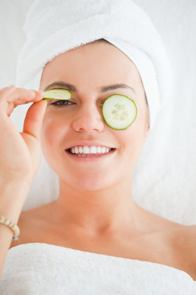 Young woman with a knowing smile with cucumber slices on the face in a spa