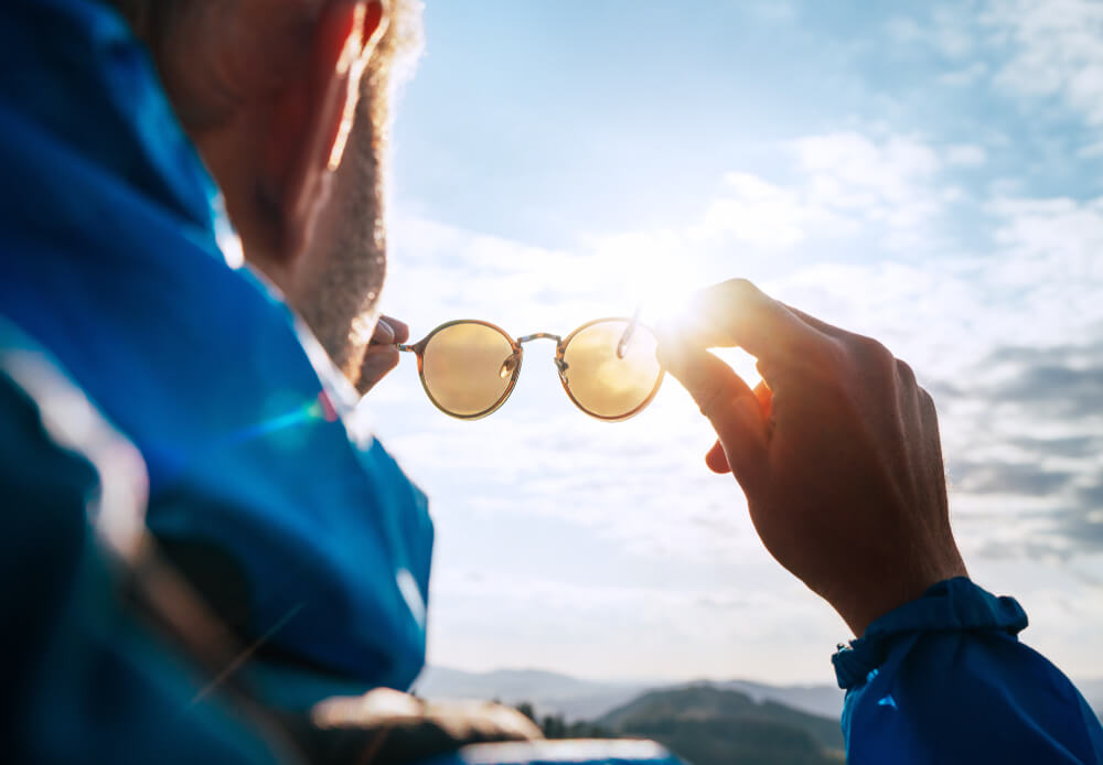 Backpacker Man Looking at Bright Sun Through Polarized Sunglasses Enjoying Mountain Landscape