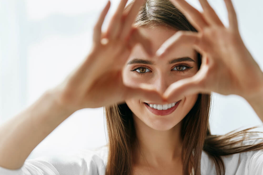 Portrait of a woman holding heart shaped hands near eyes.