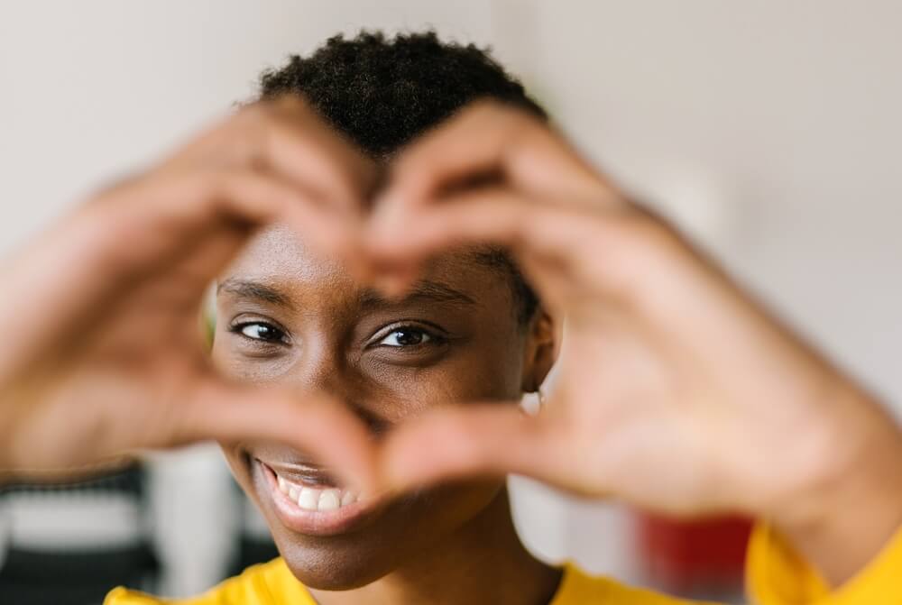 Portrait of young woman showing shape heart with hands and looking through it.