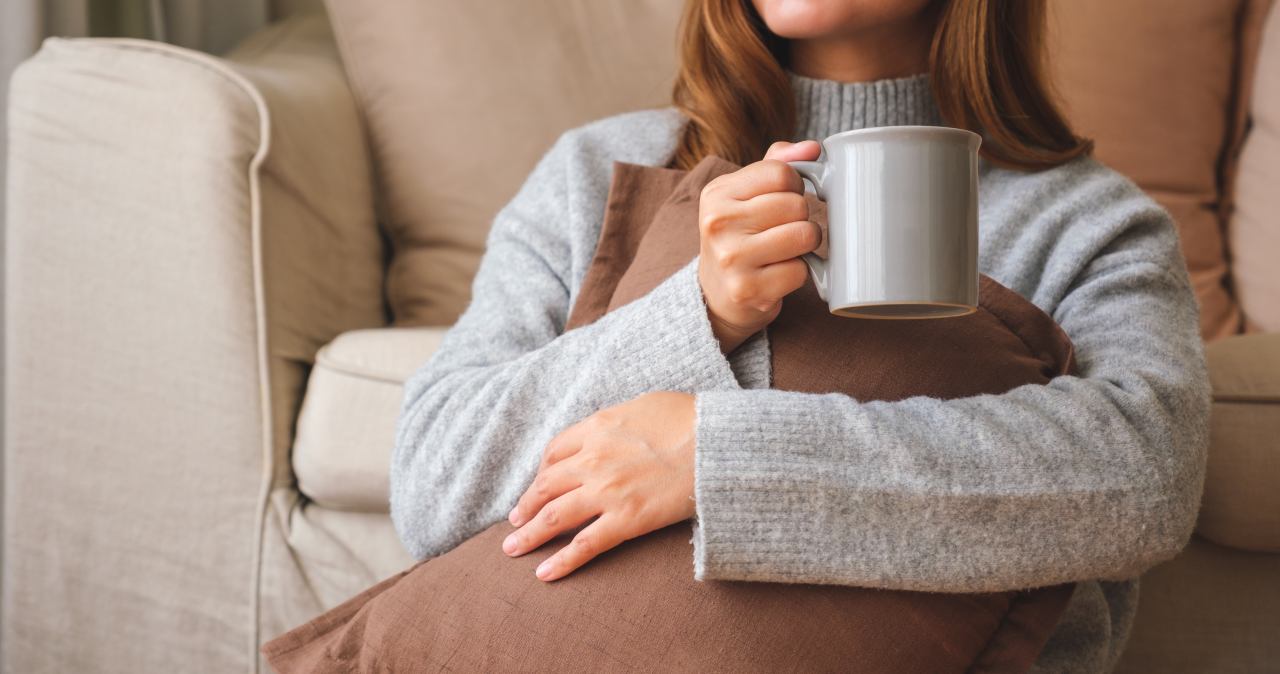 Woman in a cozy grey sweater relaxing in an armchair with a warm mug, illustrating a comfortable return to daily life during post-surgery recovery.